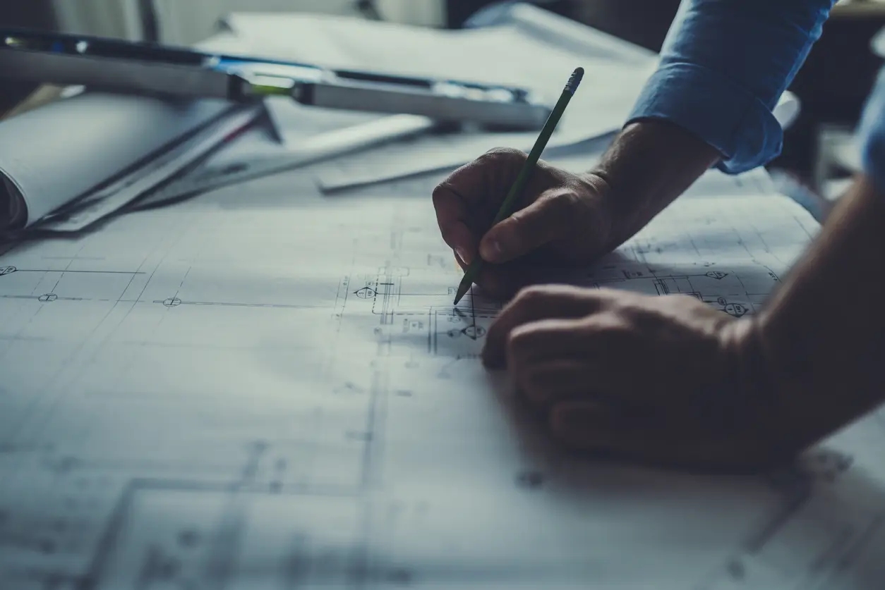 A close up of an engineering drawing with an engineer's hand working on a blueprint