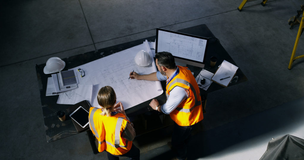 A high angle shot of two engineering going over a blueprint together in an industrial work setting.