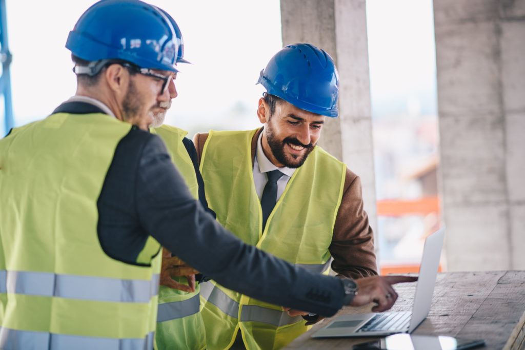 Group of engineers and facility managers in a construction site looking at a laptop while accessing documents through the use of reliable FM software.