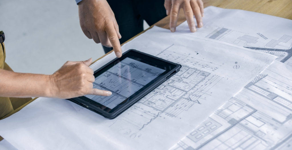Architects using a tablet computer and blueprints to look at digitized facility drawings of their current project.