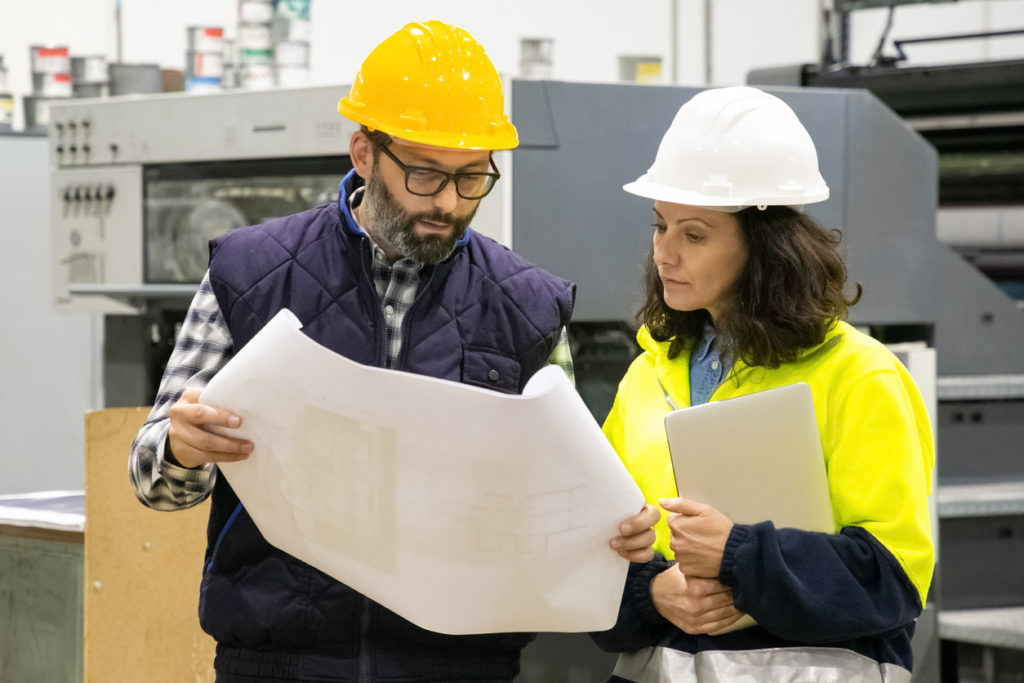 Facility manager checking a building blueprint with an auditing expert - auditing buildings concept.